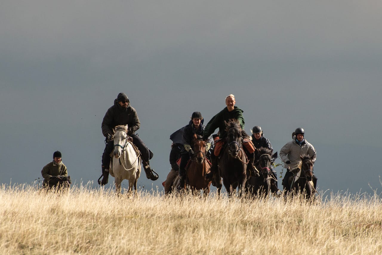 Grupo de jinetes cabalgando en una colina al atardecer